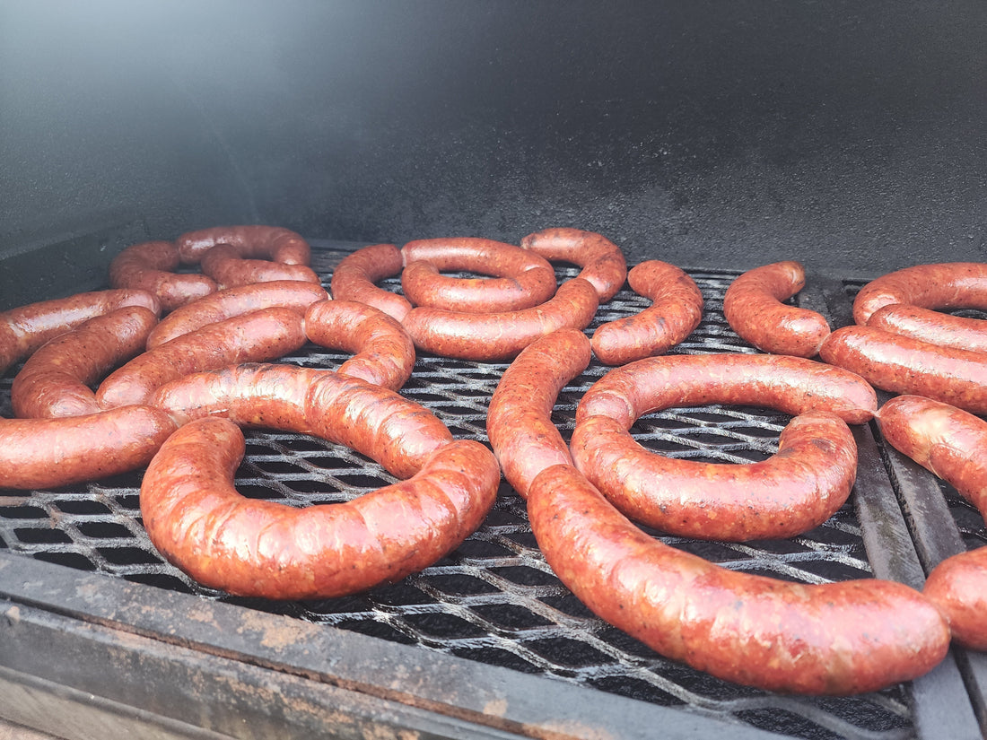 Hand-stuffed jalapeño and cheddar beef sausages smoking on a charcoal grill grate with perfect casing snap.