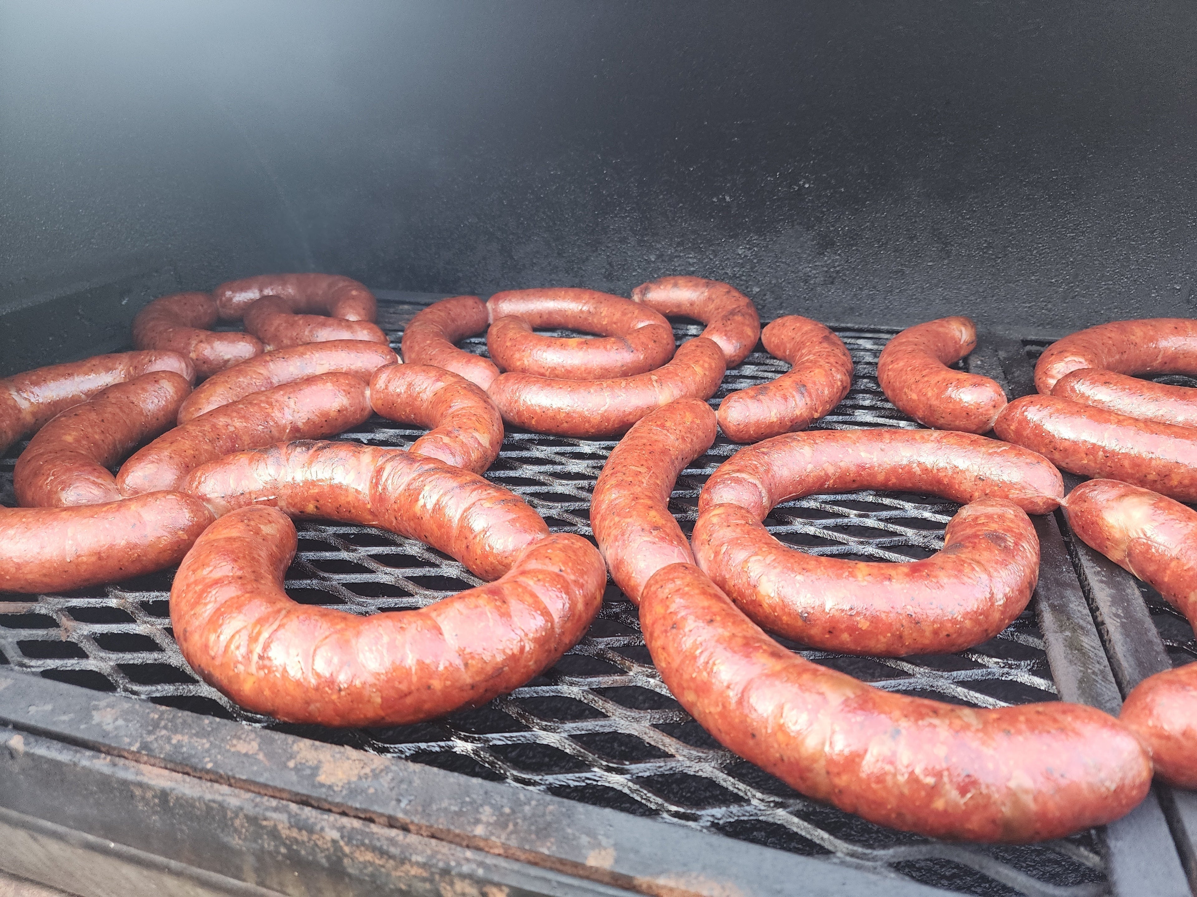 Hand-stuffed jalapeño and cheddar beef sausages smoking on a charcoal grill grate with perfect casing snap.